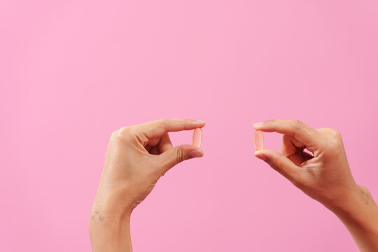 Gracefully, woman hand cradles a bottle of cod liver oil against a pink backdrop, representing health, nutrition, and the benefits of omega-3 supplementation.
