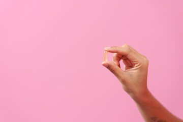 Gracefully, woman hand cradles a bottle of cod liver oil against a pink backdrop, representing...