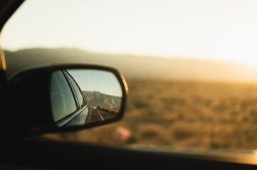Reflection of car driving down a road as seen in side-view mirror against beautiful desert...