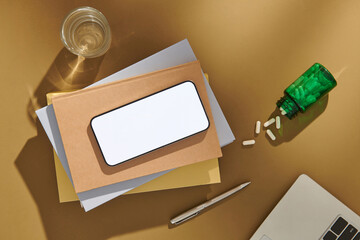 A blank screen cellphone, stationery supplies, and pills on the table