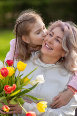 Daughter kisses mother, holding tulips outdoors