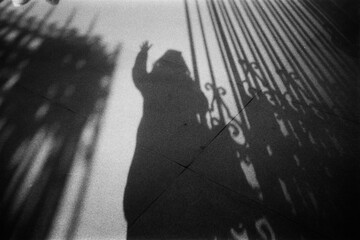 Film photography of shadow of unrecognizable person standing by gate