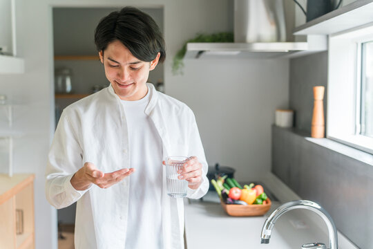 キッチンで内服薬・サプリ・医薬品を飲む病気の男性・投薬
