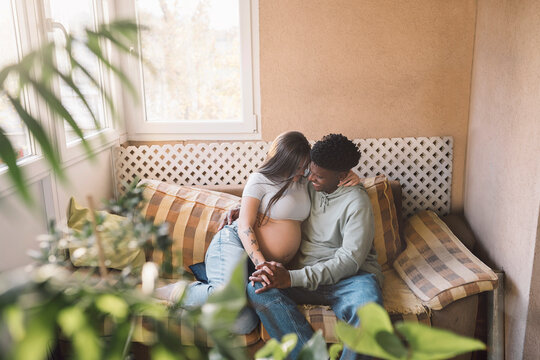 Diverse pregnant couple In Love Cuddling On The Sofa - Powered by Adobe
