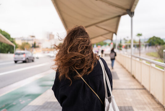 Back view of a young woman with long curly hair walking in the city