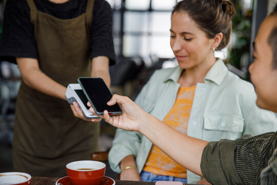 Man scanning smart phone on card reader for paying online at cafe 