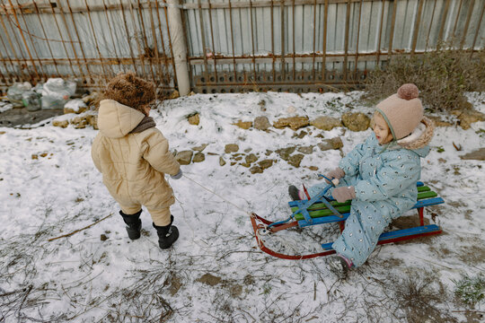 little boy pushing his sister on a sled
