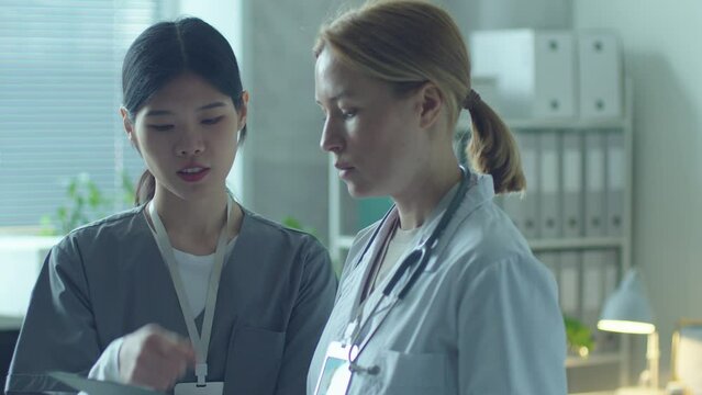 Female Caucasian doctor discussing medical records with young Asian nurse when working together in clinic