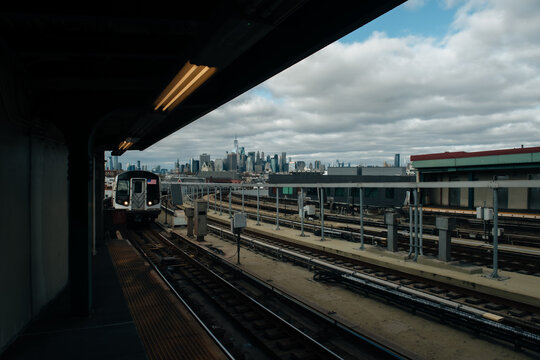NYC elevated subway station with Manhattan skyline behind
