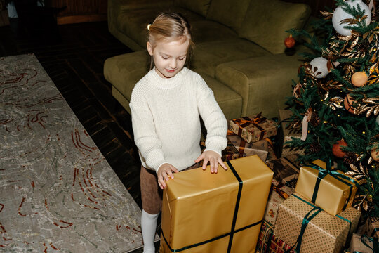 Little girl opening big gift near Christmas tree