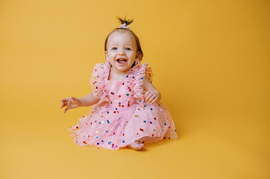 happy baby in dress on yellow backdrop