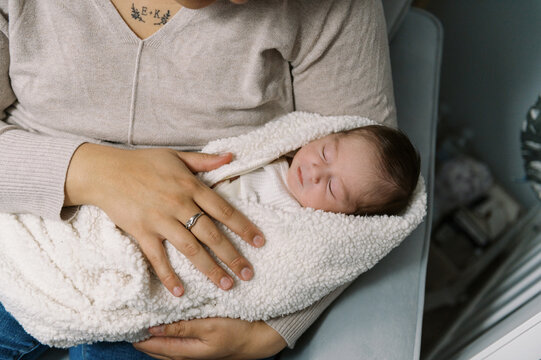 little newborn in mothers arms and wrapped in swaddle blanket
