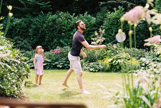 smiling daughter watching dad play badminton in garden in summer