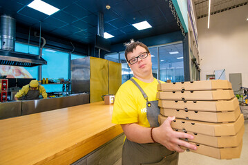Young man with Down syndrome serves pizza in a pizzeria