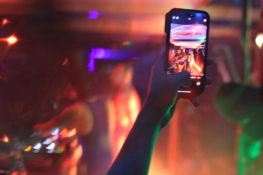 Raised hand holding mobile phone taking picture at electronic party