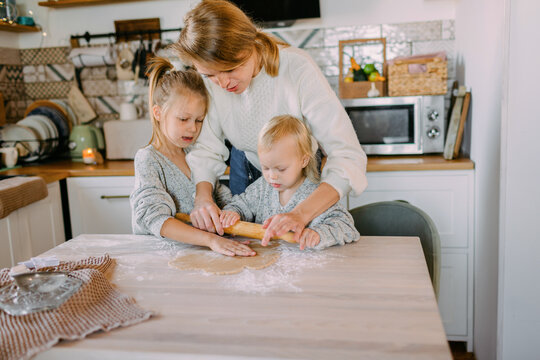 Mother rolling out the dough with her two daughters in the kitchen