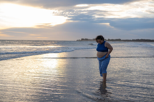 Portrait of beautiful pregnant woman standing on the beach at sunset.