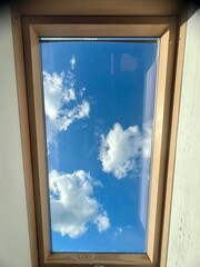 Window with blue sky and white clouds in the attic of the house
