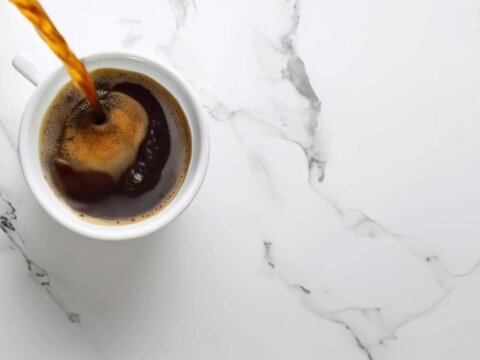 Black coffee pouring into white mug on white marble tabletop