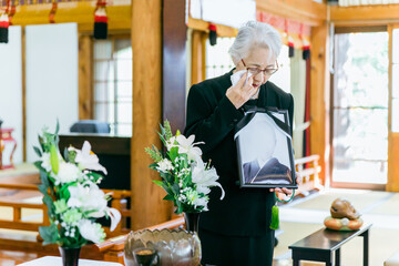お葬式で遺影を持って挨拶する喪主の高齢者女性（喪主の挨拶・泣く）

