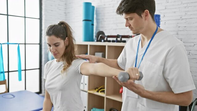 A female patient performs rehabilitation exercises under the guidance of a male physiotherapist in a clinic room.