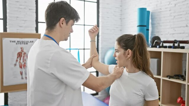 Therapist man assisting patient woman in sunny physiotherapy clinic room practicing arm rehabilitation.