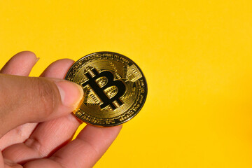 a close up hand holding a bitcoin on a yellow background and with space for text,web3 exchange and blockchain concept
