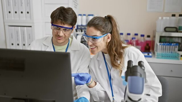 Two scientists, a man and a woman, analyze data on a computer in a modern laboratory setting.