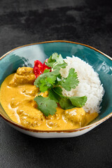 Traditional indian food. Chicken curry with boiled rice in ceramic bowl on black concrete background. Asian curry with chicken and basmati rice on dark stone table. Hot dish - spicy curry.