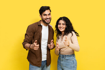 Young couple giving thumbs up against a yellow background, conveying approval, positivity, and...