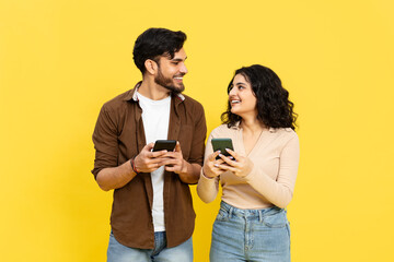 Happy Couple Sharing Content On Smartphones Against Yellow Background, Online Communication, Social Media, Tech Lifestyle, Casual Clothing, Young Adults, Smiling, Connectivity, Vibrant