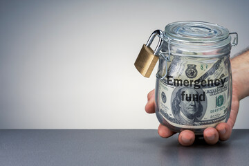 Hand holding money in the jar with lock. Man holding glass jar with dollar banknotes on grey...