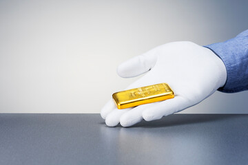 Man holding gold bar against grey light background with free space for text, closeup.