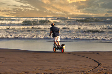 Guy riding gas powered scooter towards the waves on the beach © Simon