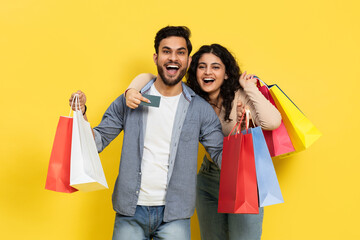 Couple Smiling And Holding Colorful Shopping Bags And A Credit Card, Exemplifying Consumerism,...