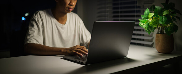 Cropped shot of male freelancer in casual clothes working with laptop at night .