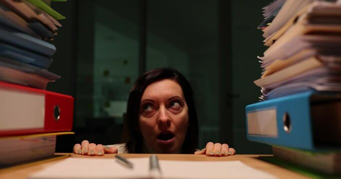 Stressed businesswoman hides behind stacks of documents and feels overloaded with work