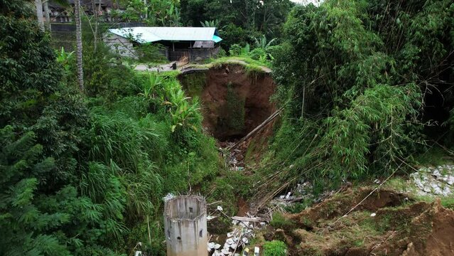 After earthwork, rainy season caused soil erosion and roadbed was affected. Part of road collapsed, empty sinkhole at place seen of roadway. Aerial shot of calamity at rural area of Bali island