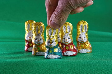 Easter chocolates, hand holding single easter bunny, bunnies on a green background.