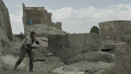 Sneaking man with toy gun being blown up in ruined area - slow motion