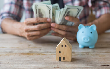 Hand's man holding money behind small house,saving concept,soft focus.