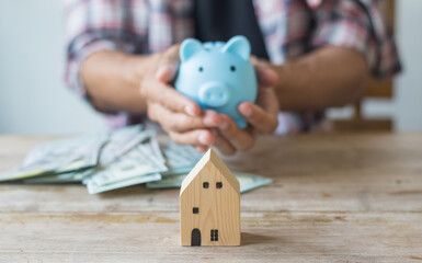 Hand's man holding money behind small house,saving concept,soft focus.