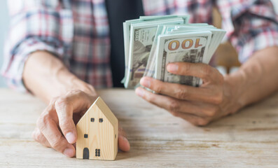 Hand's man holding money behind small house,saving concept,soft focus.