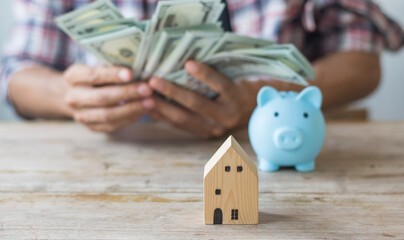 Hand's man holding money behind small house,saving concept,soft focus.