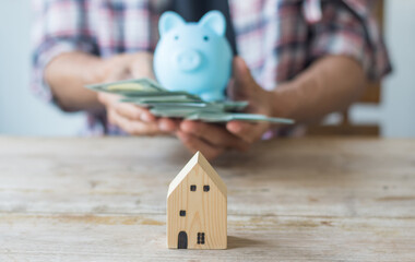 Hand's man holding money behind small house,saving concept,soft focus.