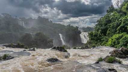 The streams of a turbulent river foam on the rocks. Lush tropical vegetation on the rocks. The...