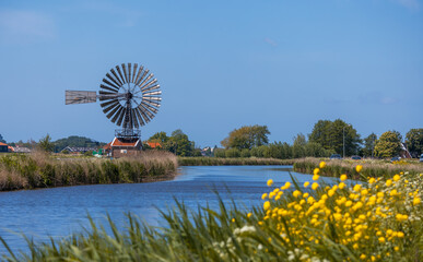 Scenic view of small windmill by the canal and wildflowers in the Netherlands country side