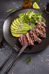 grilled cooked piece of tuna fillet with sliced avocado and salad on black ceramic plate