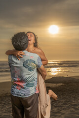 Man carrying hugging his girlfriend laughing on the beach at sunset time