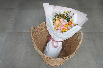 Mixed colorful flower bouquet in basket on gray tiled floor background